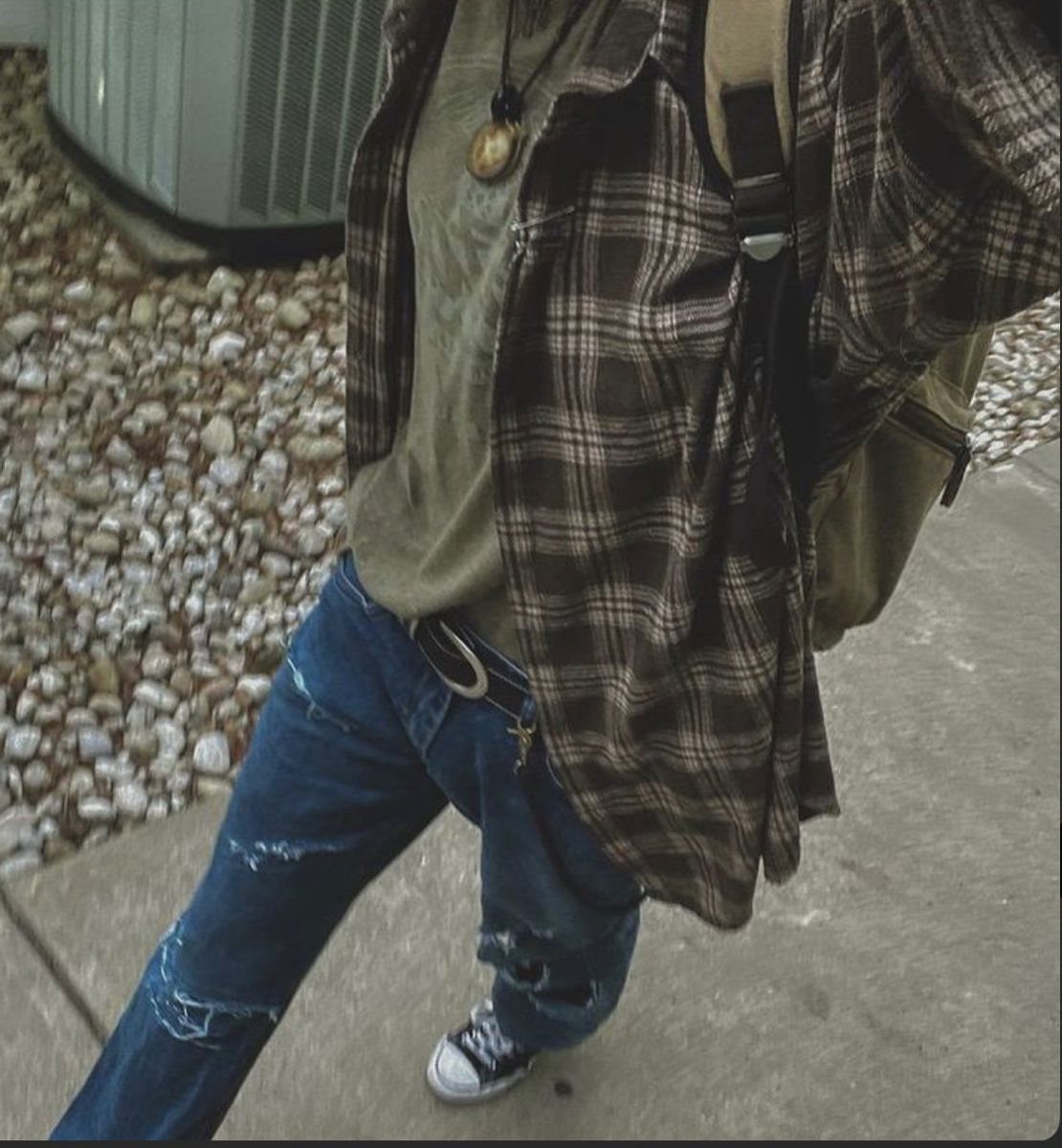 A person wearing a brown plaid flannel shirt, olive t-shirt, and distressed blue jeans.