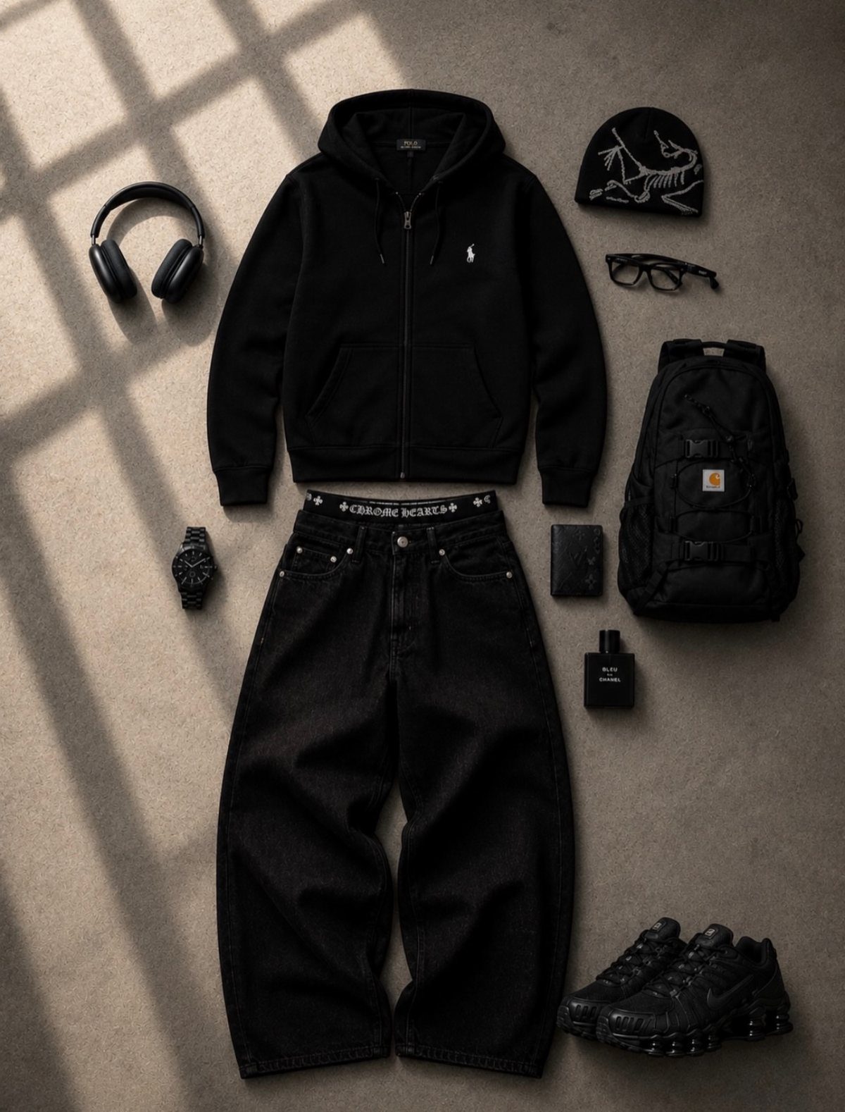Black streetwear clothing and accessories including a hoodie, baggy jeans, headphones, and sneakers laid flat on a tan background.
