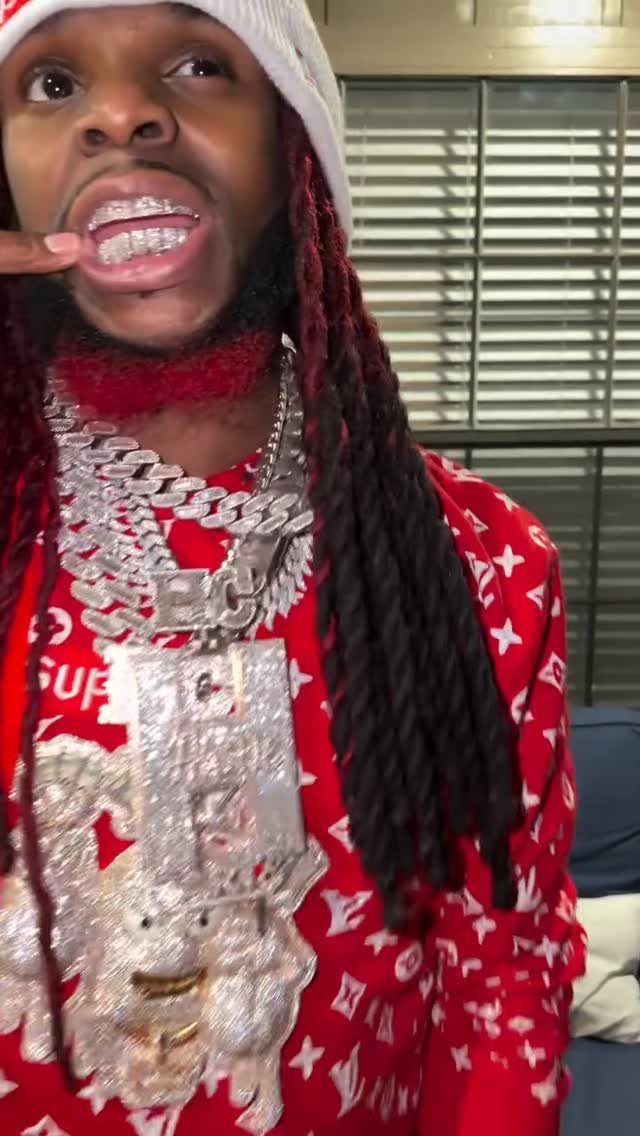 A man with red dreadlocks wearing heavy diamond chains and showing his diamond grillz.