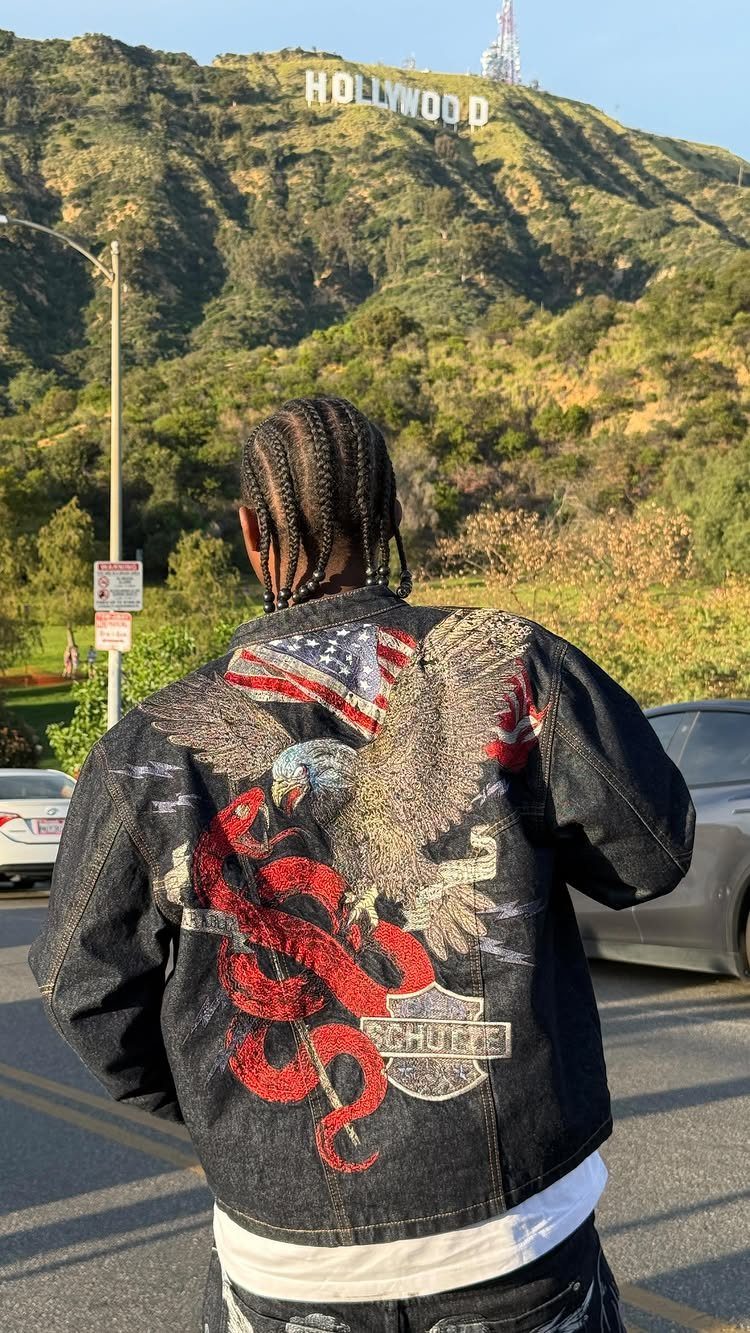 Person wearing a black denim jacket with large eagle embroidery facing the Hollywood sign.
