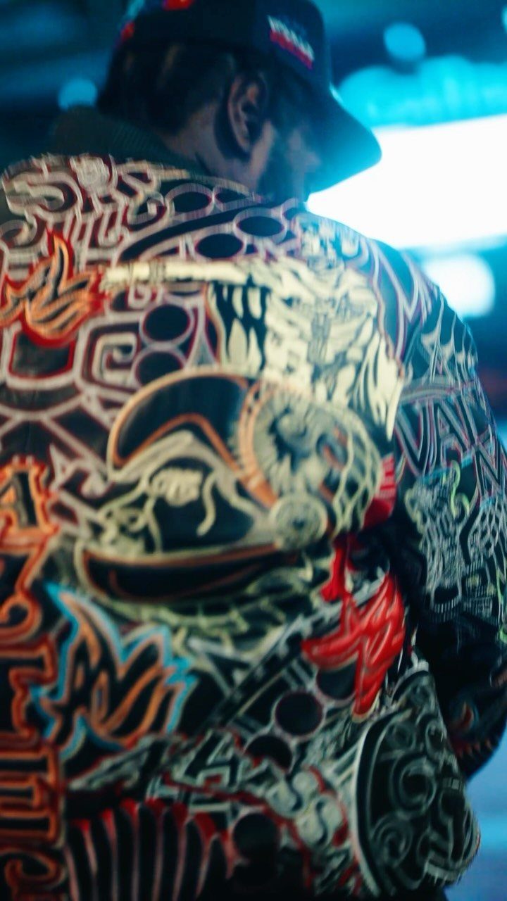 Person wearing a dark cap and a jacket with vibrant graffiti-style graphic patterns.