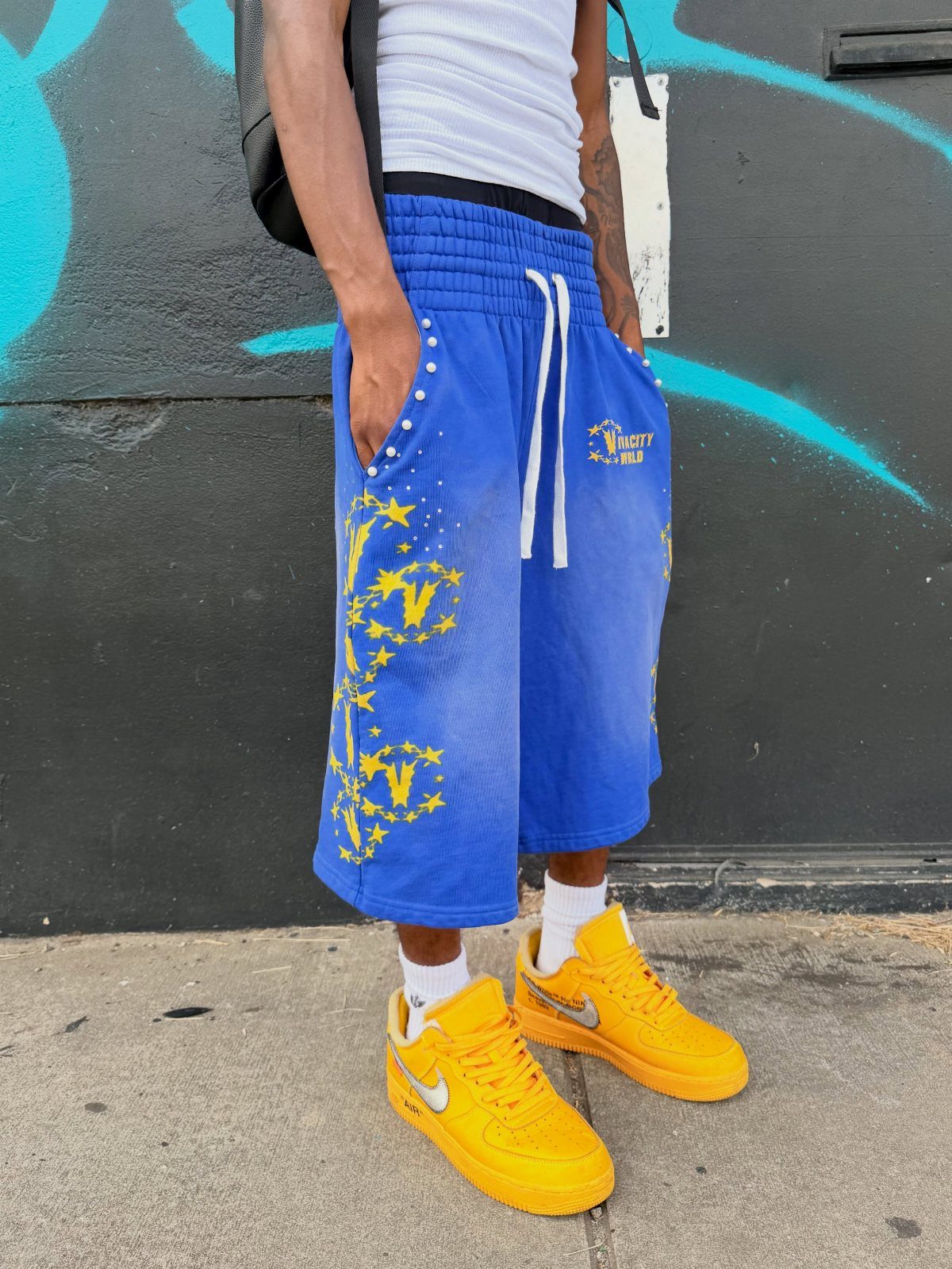 Person wearing bright blue star-patterned shorts and yellow sneakers against a graffiti wall.