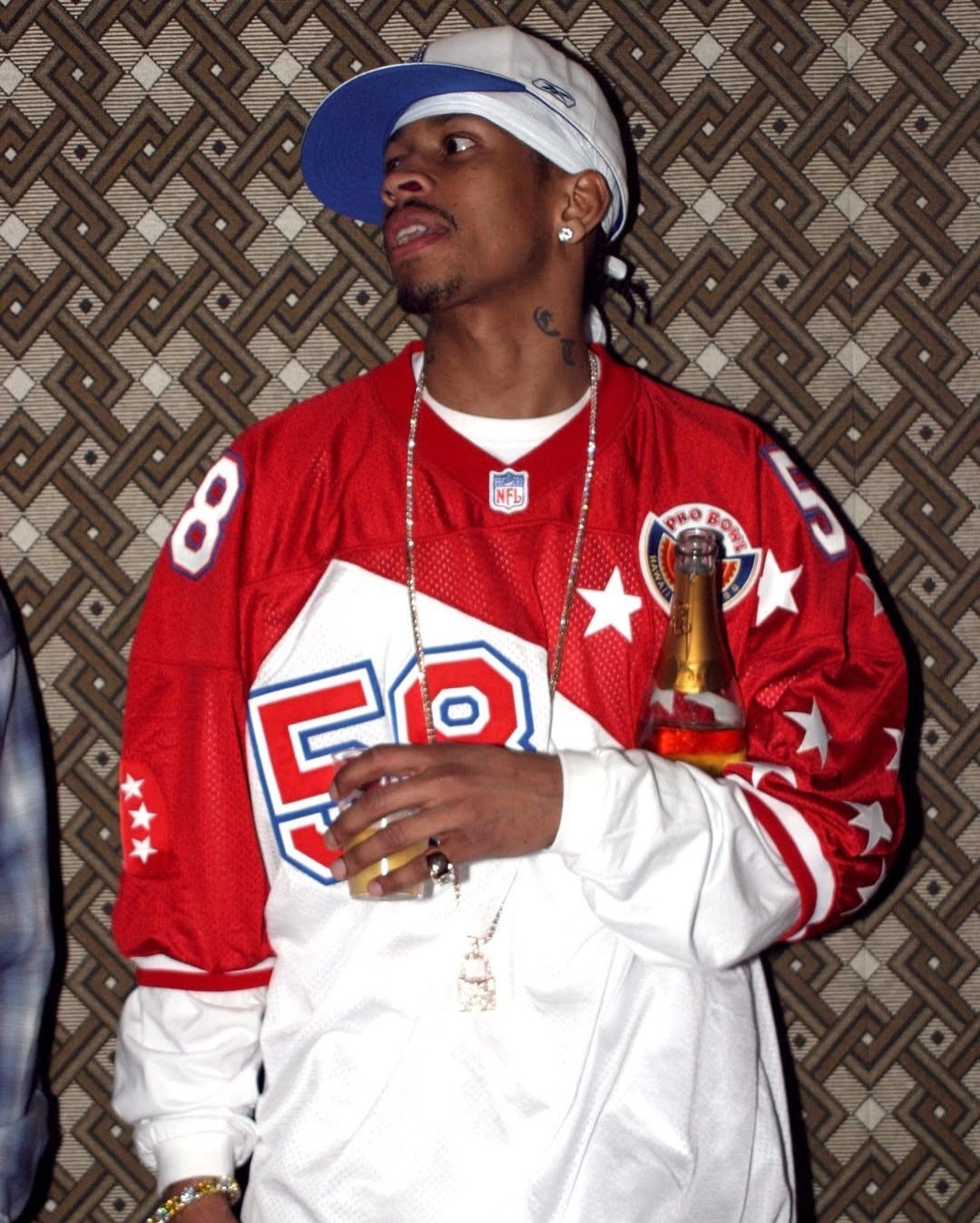 Man in oversized red and white sports jersey, baseball cap, and silver chain necklace.