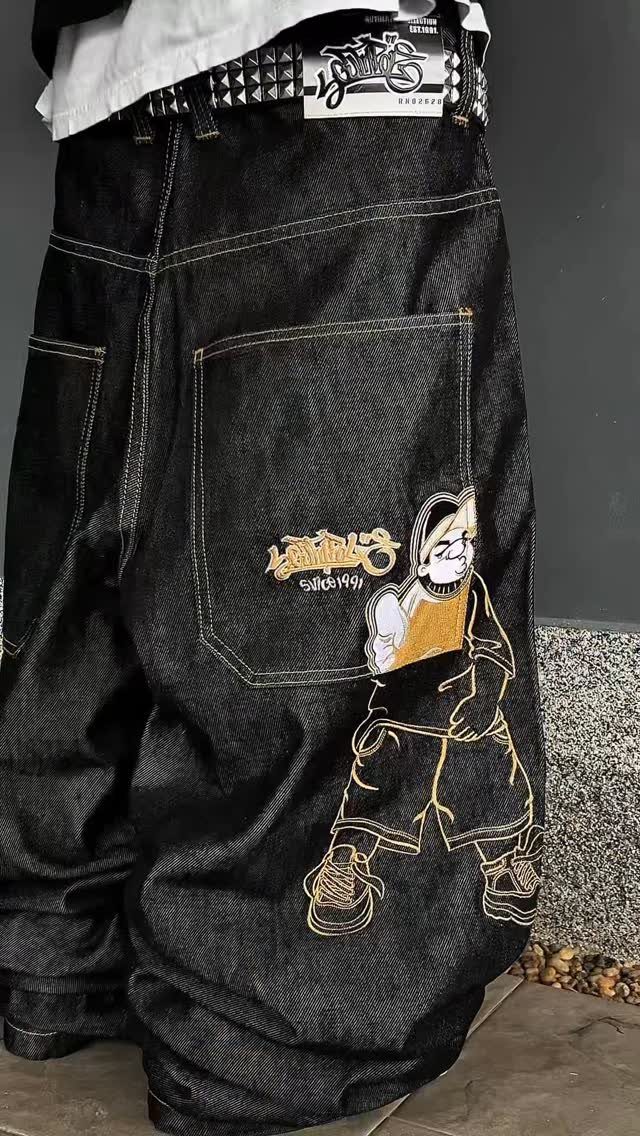 Baggy black denim jeans featuring yellow cartoon character embroidery on the back pocket.