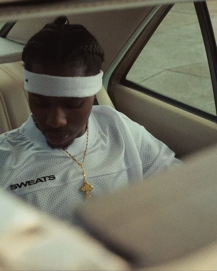 A man in a white mesh shirt and headband sitting in a car.