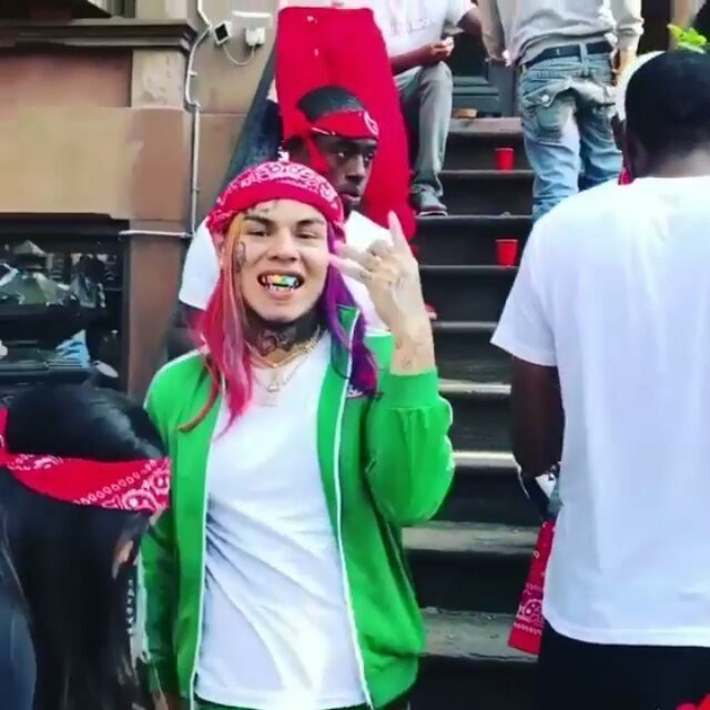 Person with pink hair wearing a red patterned bandana and a green hoodie.