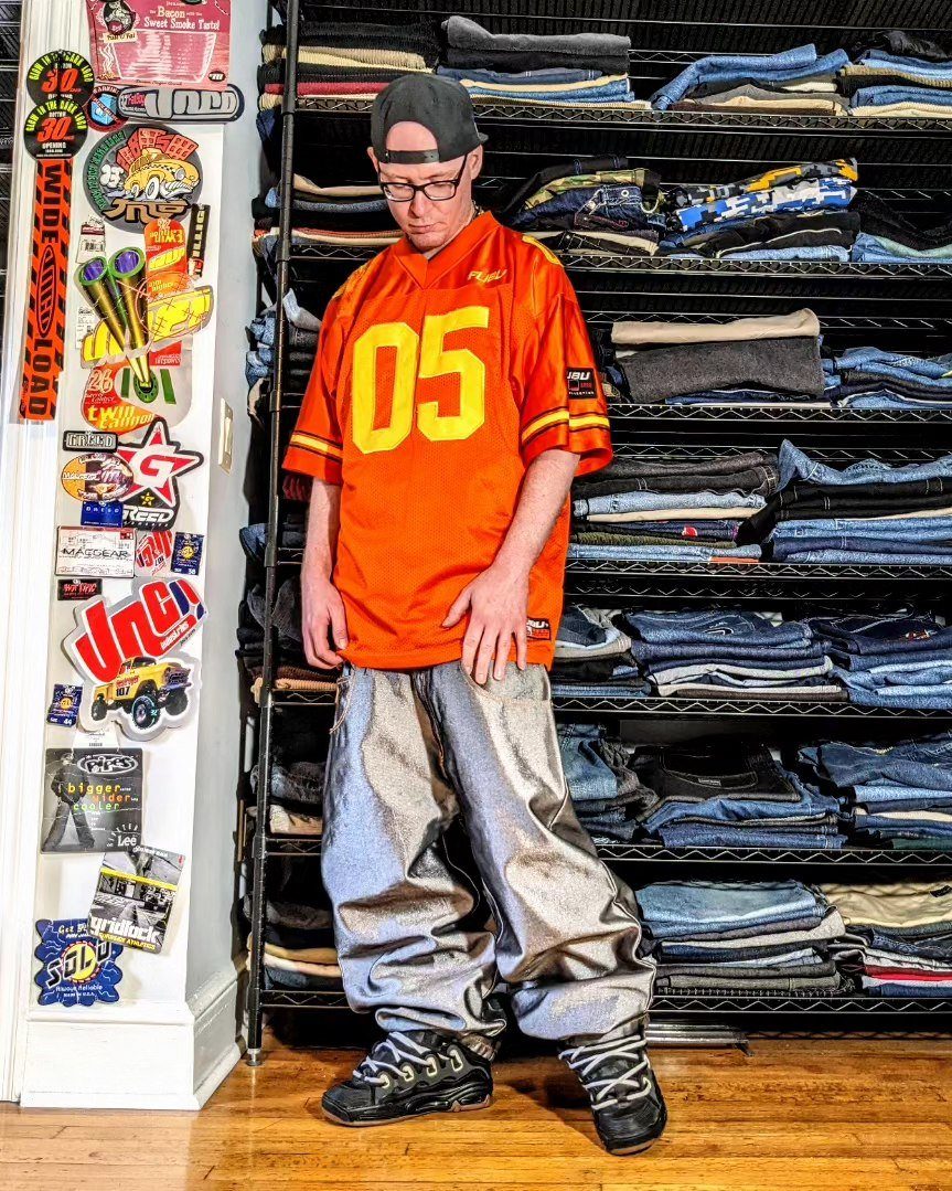 Man wearing an orange jersey and baggy silver metallic pants standing in a clothing store.