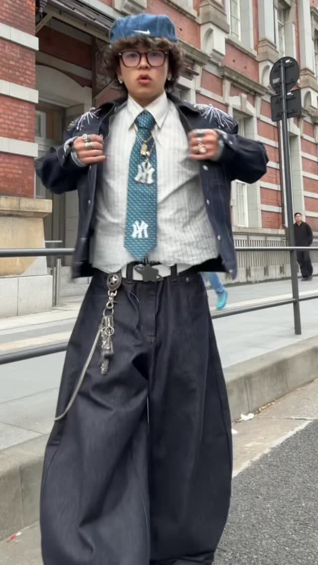 A young man in eclectic Japanese street fashion posing on a city sidewalk.