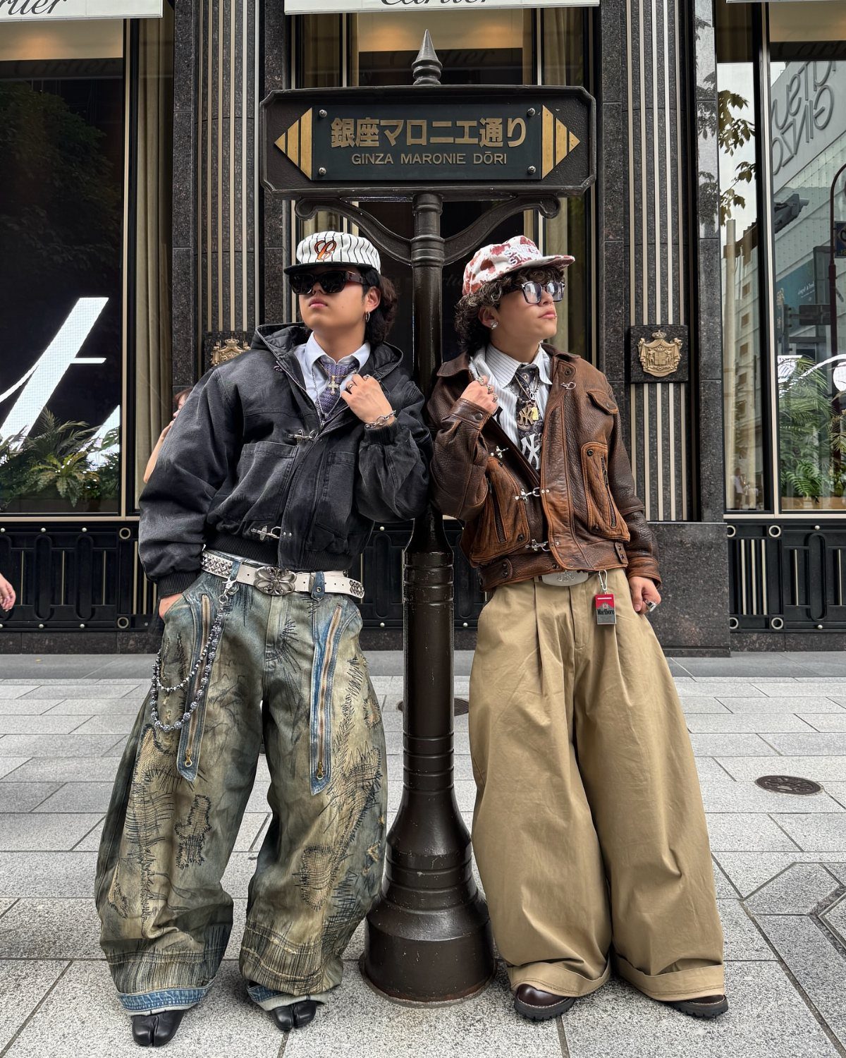 Two men posing in oversized jackets and extremely wide-legged trousers on a city street.