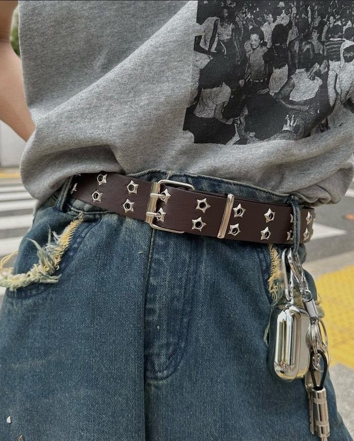 A dark brown belt with silver star grommets and hanging silver keychains on blue denim jeans.
