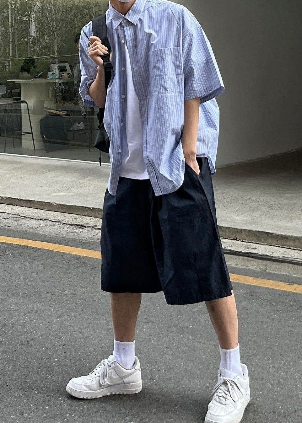 Man wearing a blue striped shirt, white t-shirt, black Bermuda shorts, and white sneakers.