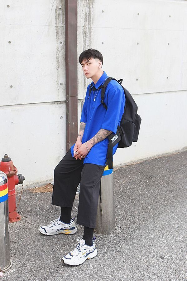 A young man in a blue shirt and black trousers wearing white chunky sneakers.