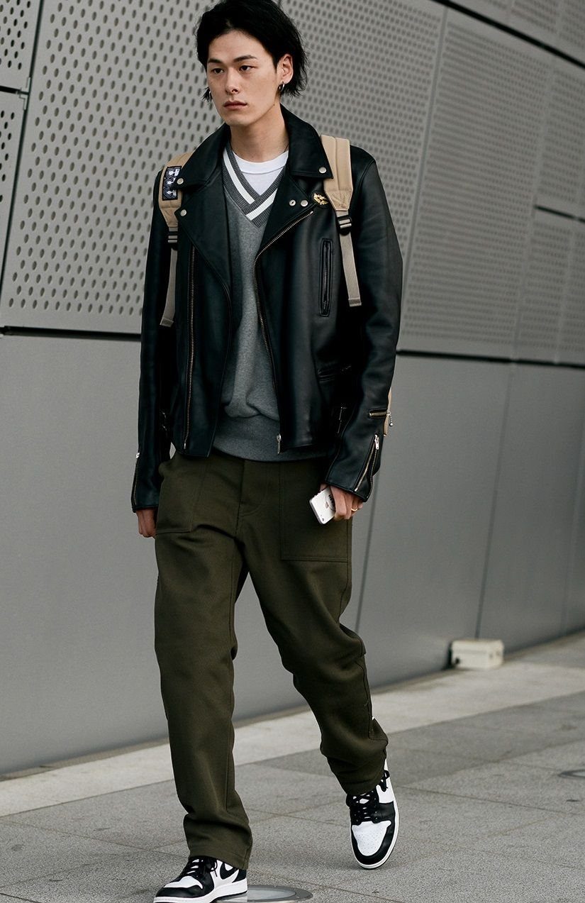 Man walking in a black leather biker jacket, grey sweatshirt, and olive green trousers.
