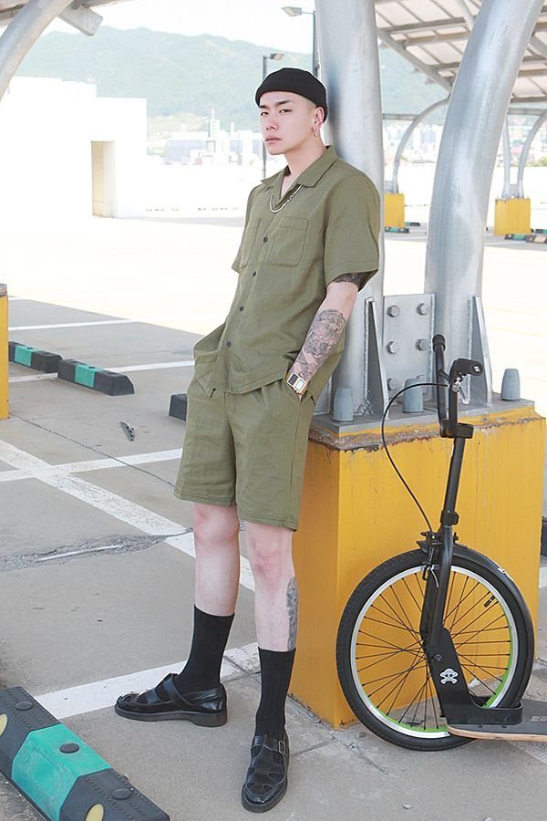 Man in olive green short-sleeve button-down shirt and matching shorts standing outdoors.