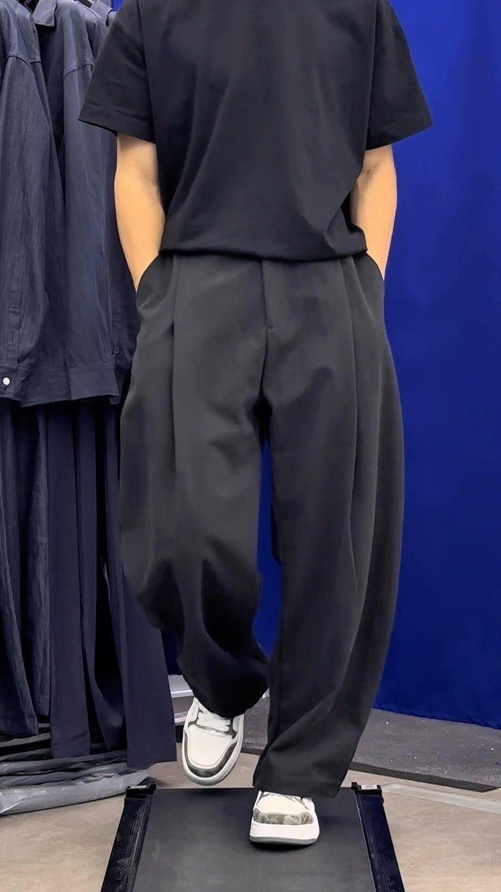 Man wearing black oversized t-shirt and pleated wide-leg trousers with white sneakers.