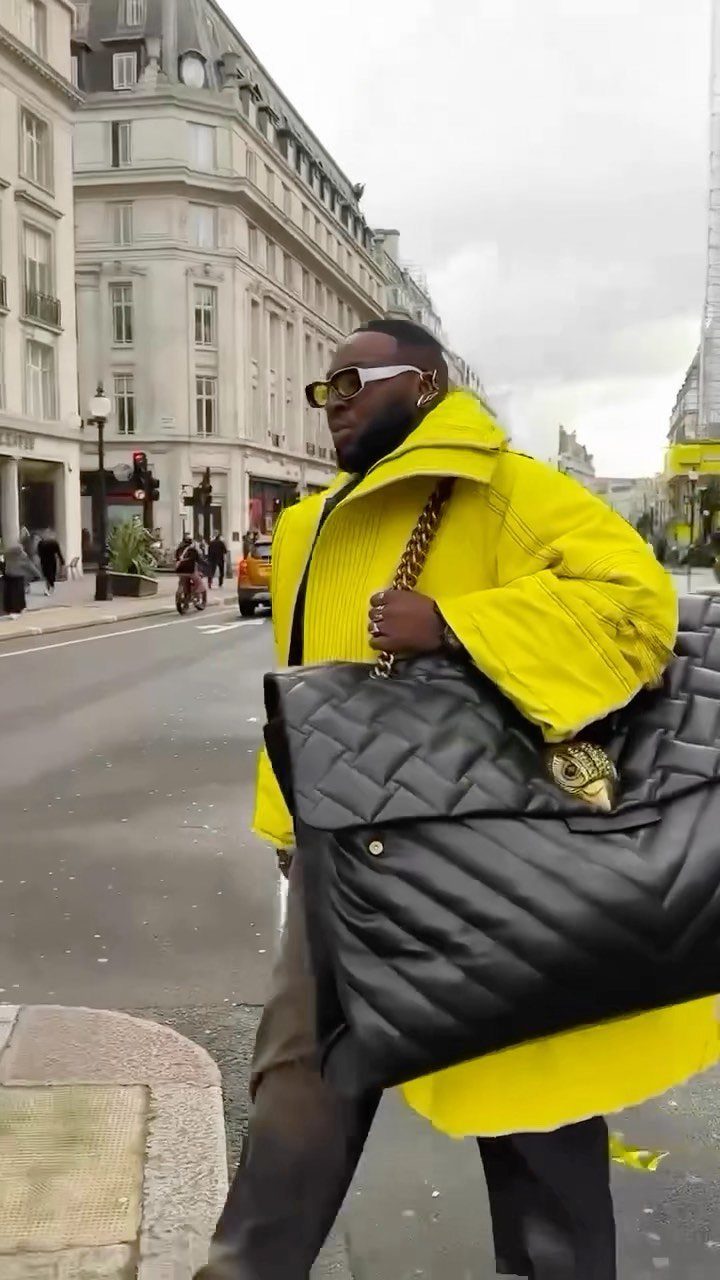 A man in a bright yellow puffer jacket and sunglasses walks through a London city street.