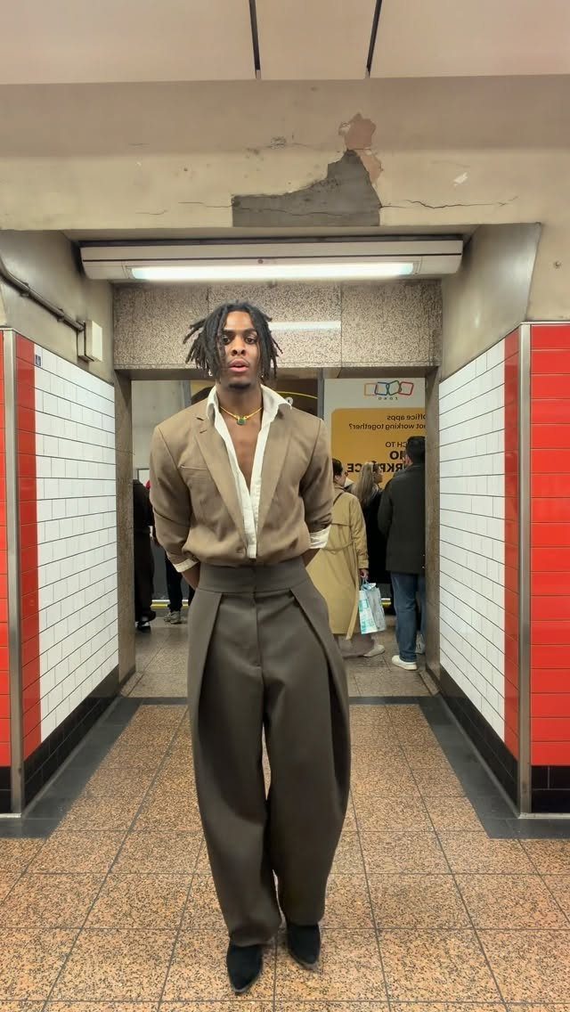 A man in stylish tan and brown clothing posing in a subway station hallway.