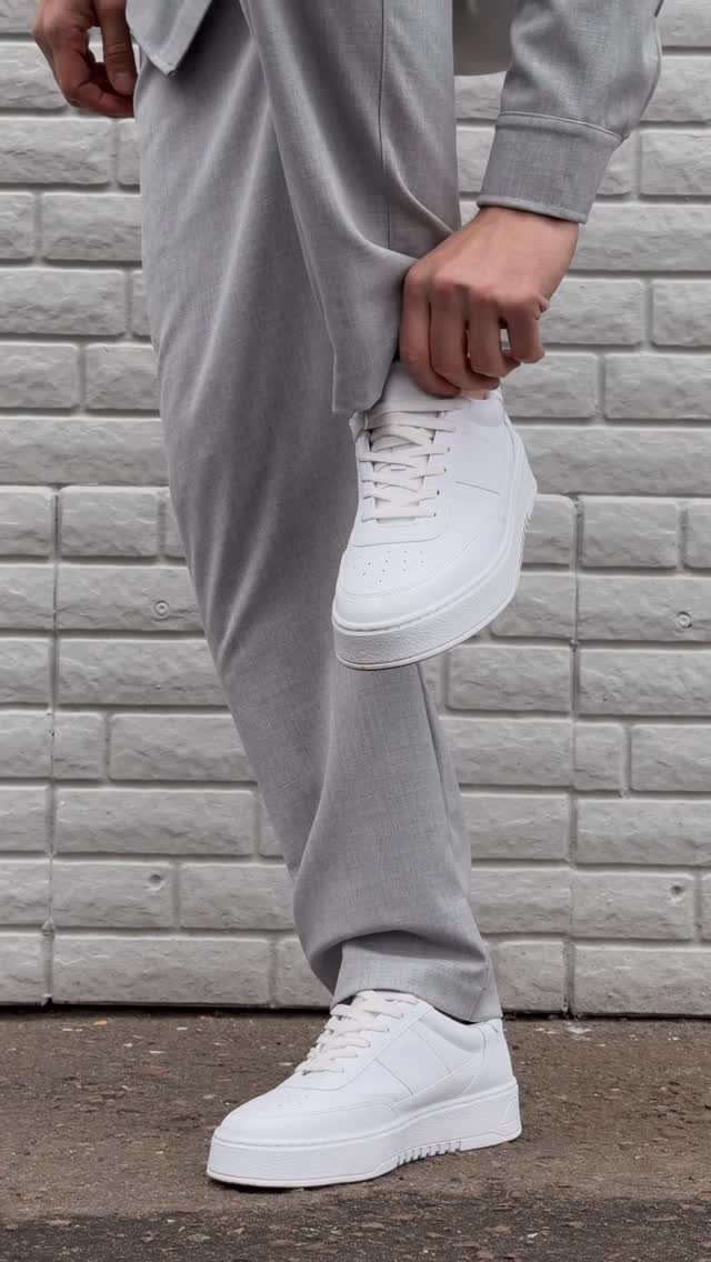 Person wearing grey sweatpants and white chunky platform sneakers against a grey brick wall.
