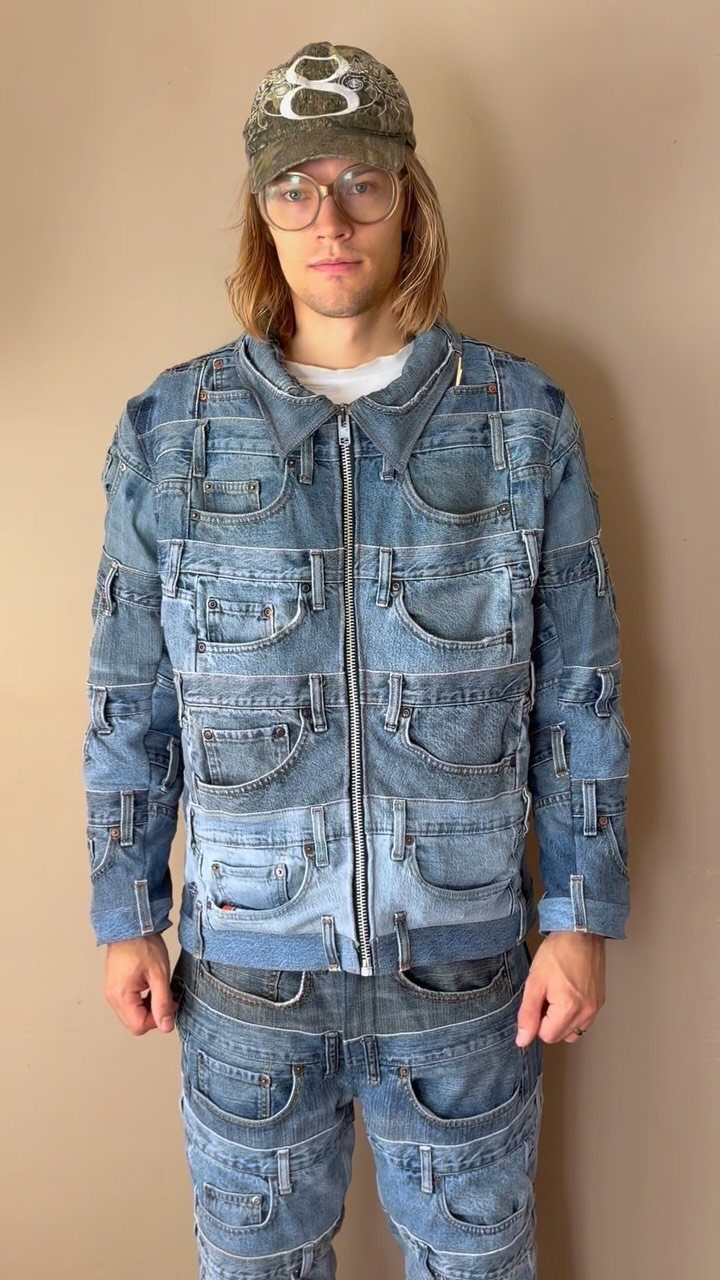 Man wearing a unique patchwork denim jacket and matching denim pants against a beige wall.