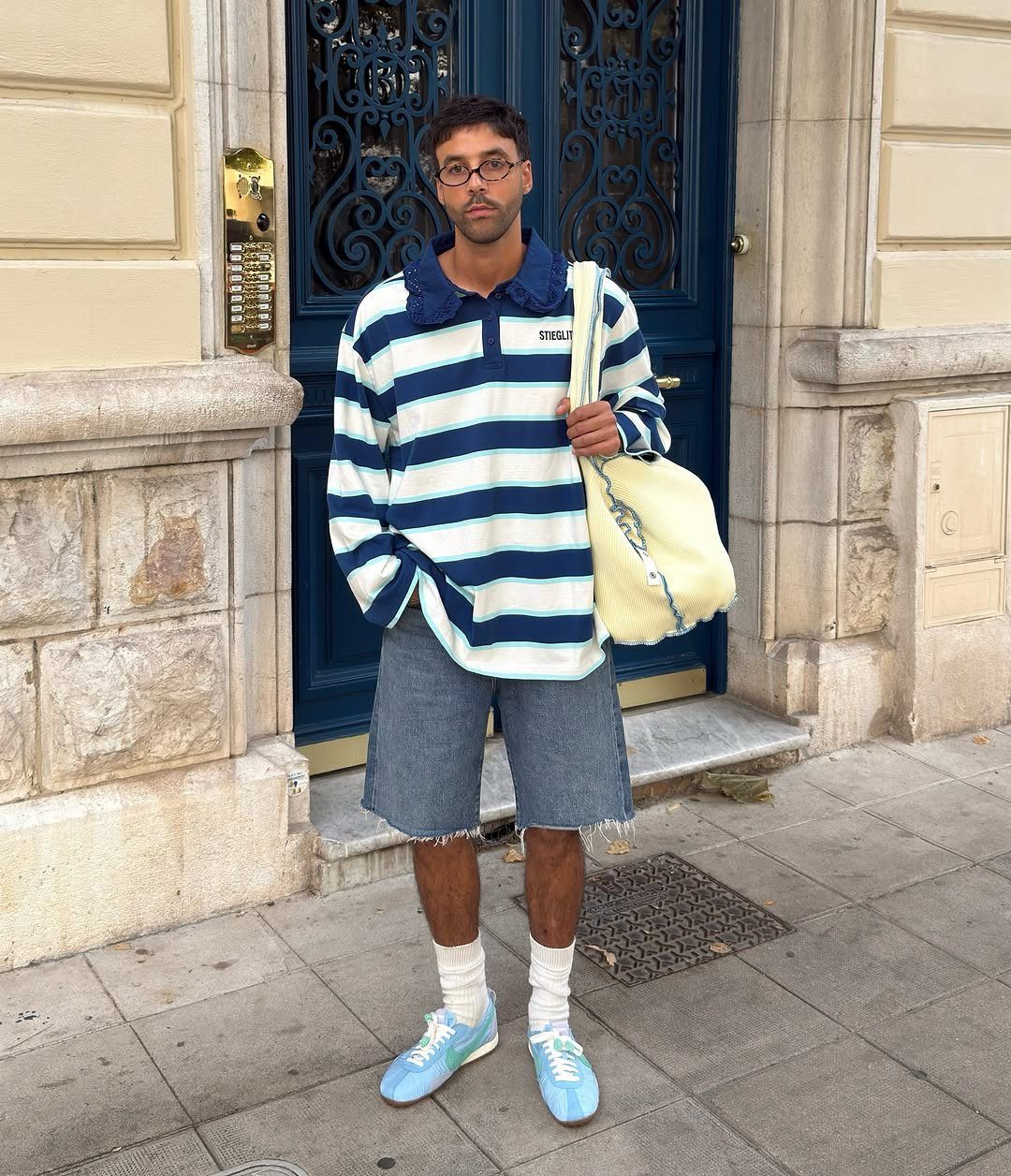 Man wearing a blue and white striped polo shirt, denim shorts, and light blue sneakers.