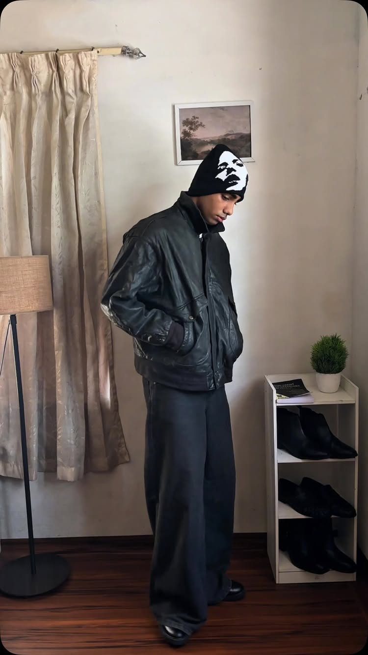 Man wearing a black leather jacket, baggy pants, and a graphic black and white beanie.