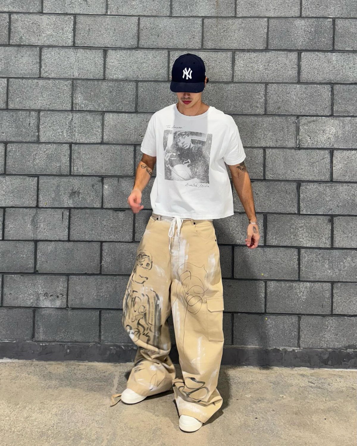 Man wearing a white graphic t-shirt and oversized beige cargo pants with paint splatters.