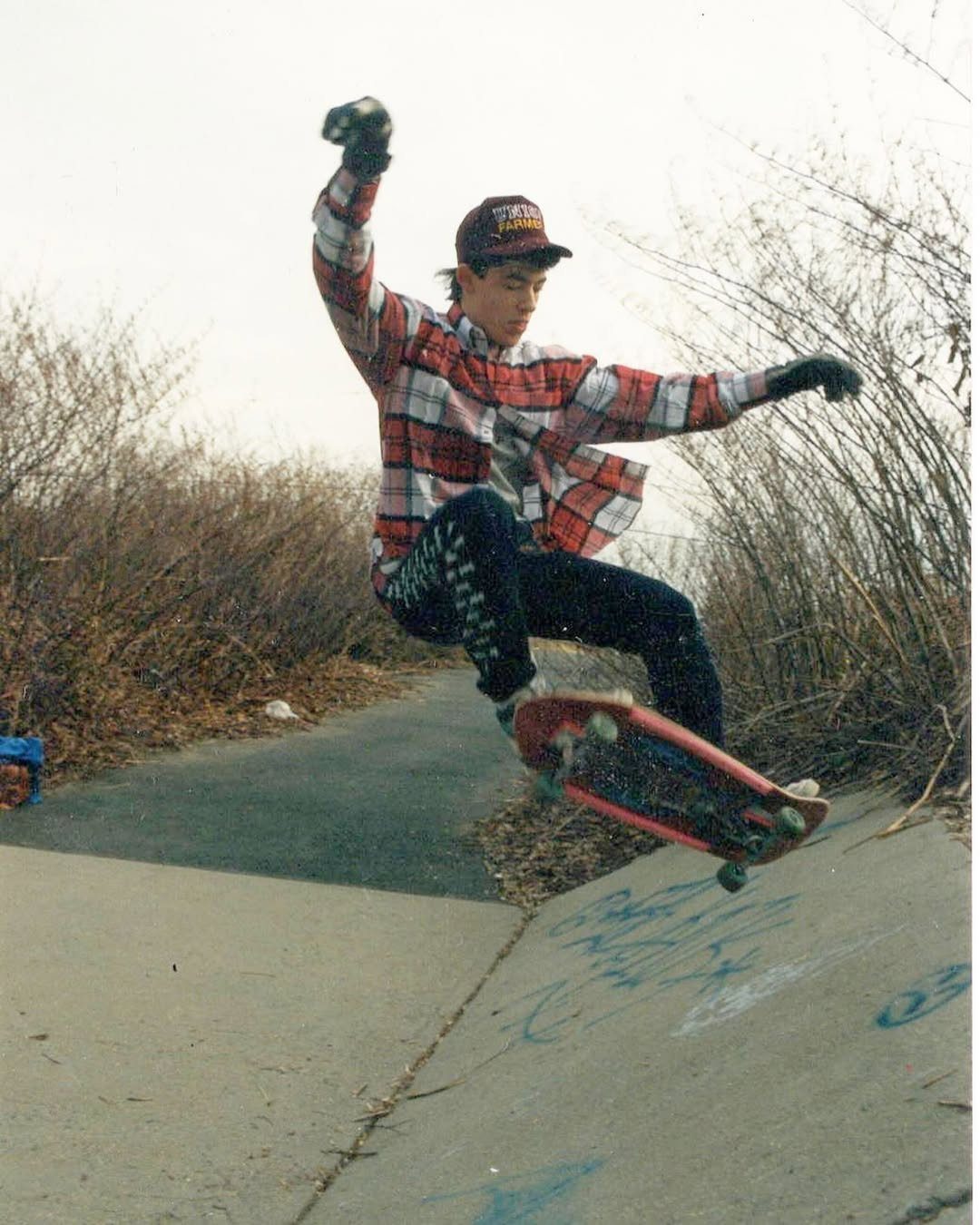 A skateboarder in a plaid flannel shirt performs a trick on a concrete path.