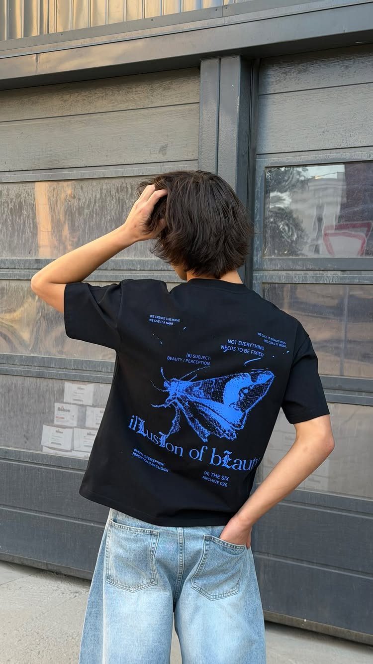 A person wearing a black oversized graphic t-shirt and light blue jeans standing outdoors.