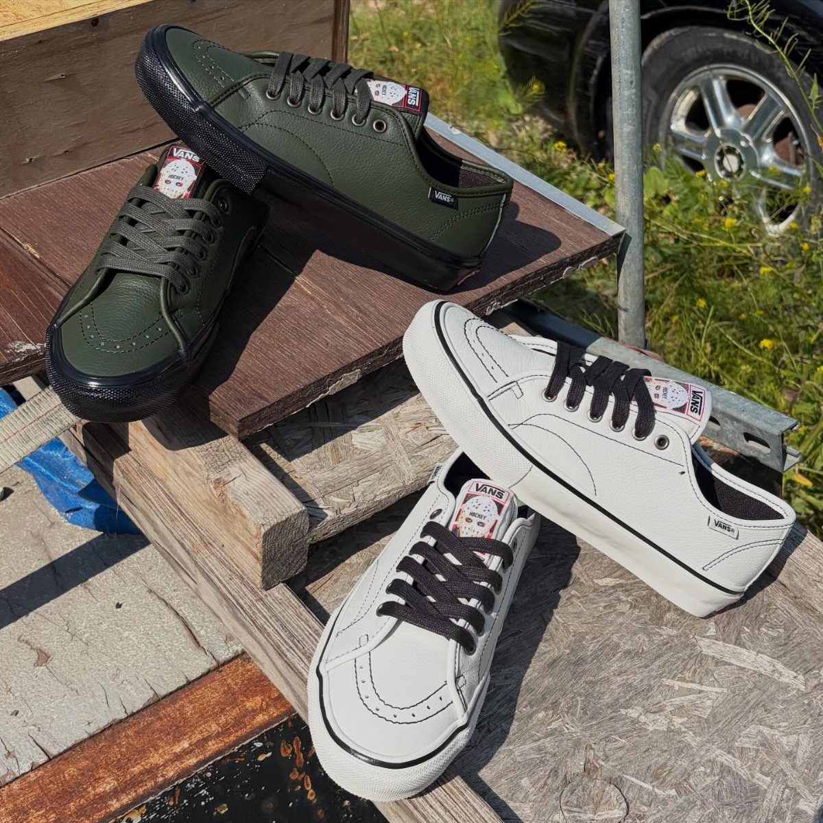 Four Vans sneakers in olive green and white resting on rustic wooden planks outdoors.