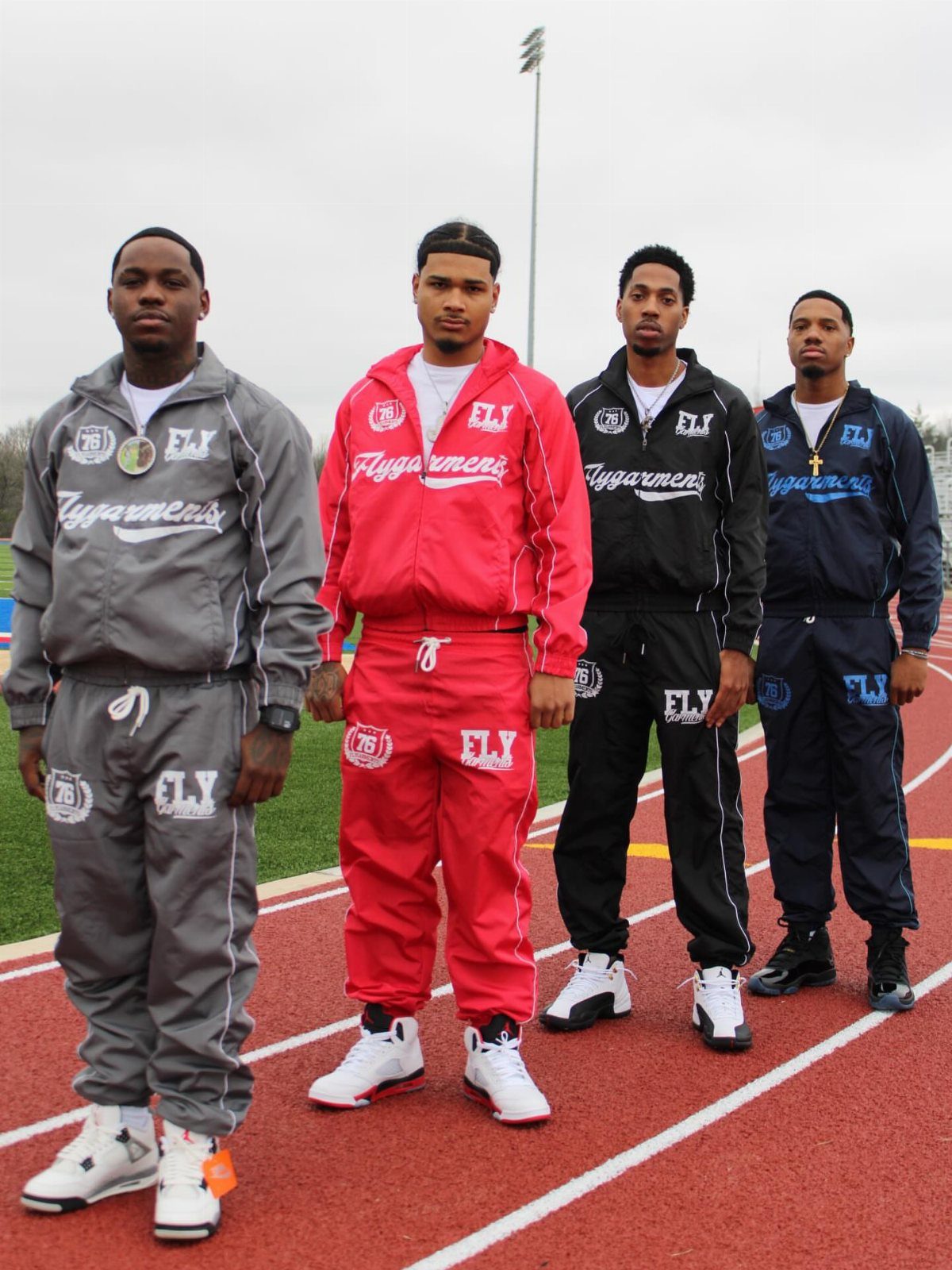 Four men posing on a running track wearing various colored matching jogger sets.