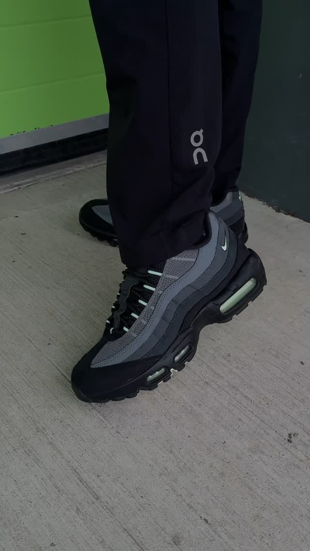 Grey and black Nike sneakers worn with black pants on a concrete ground.