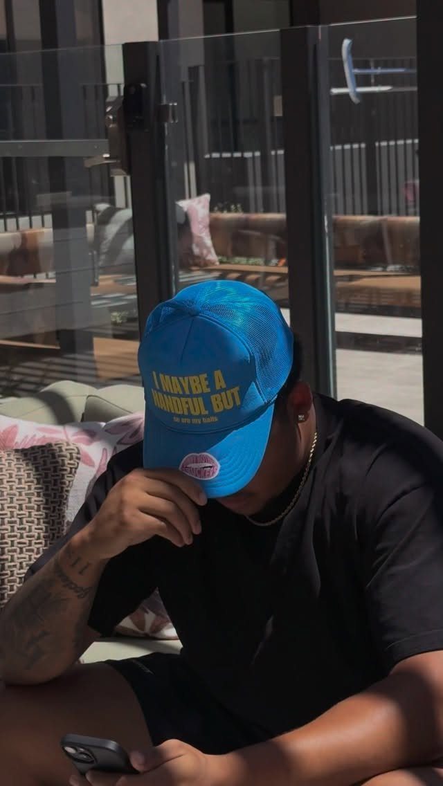 A man wearing a bright blue trucker hat with white text while sitting outdoors.