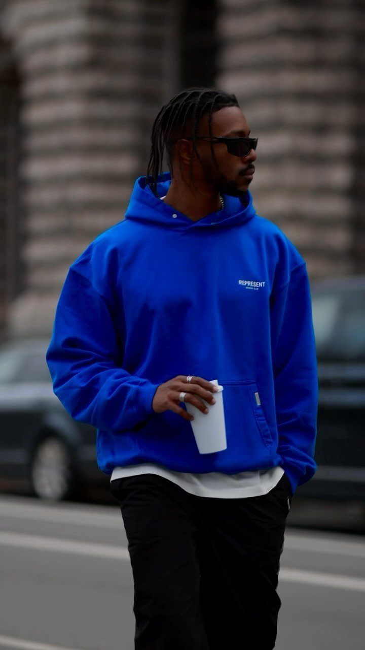 Man in a bright blue oversized hoodie and black pants walking on a city street.