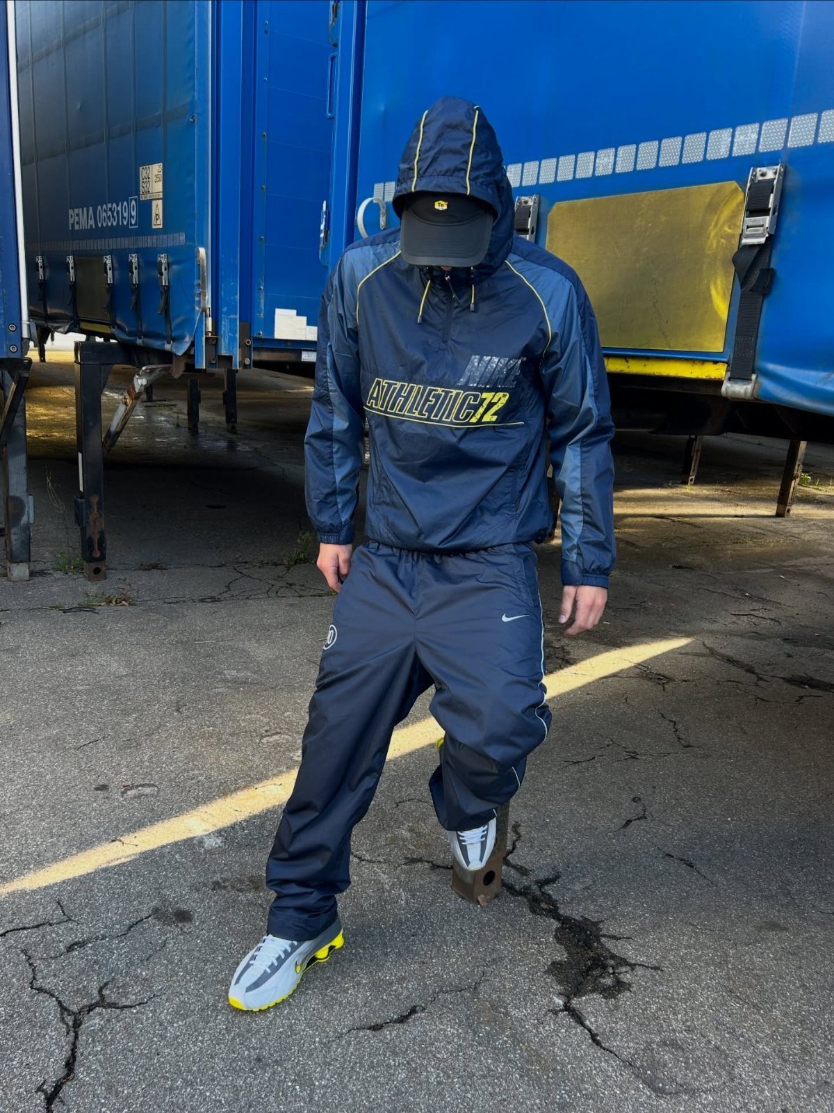 A person wearing a navy blue hooded windbreaker, matching track pants, and white sneakers.