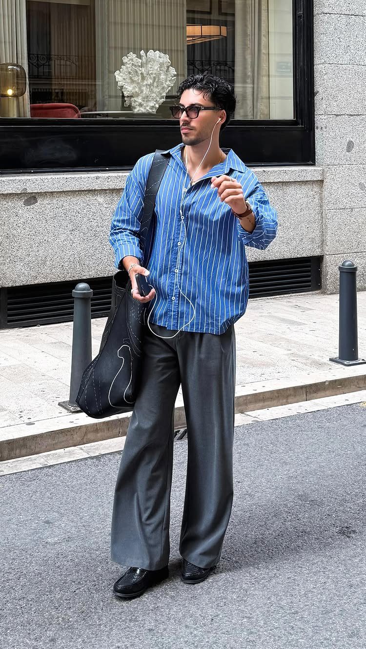 Man in a blue striped shirt and wide-leg grey trousers walking on a city street.