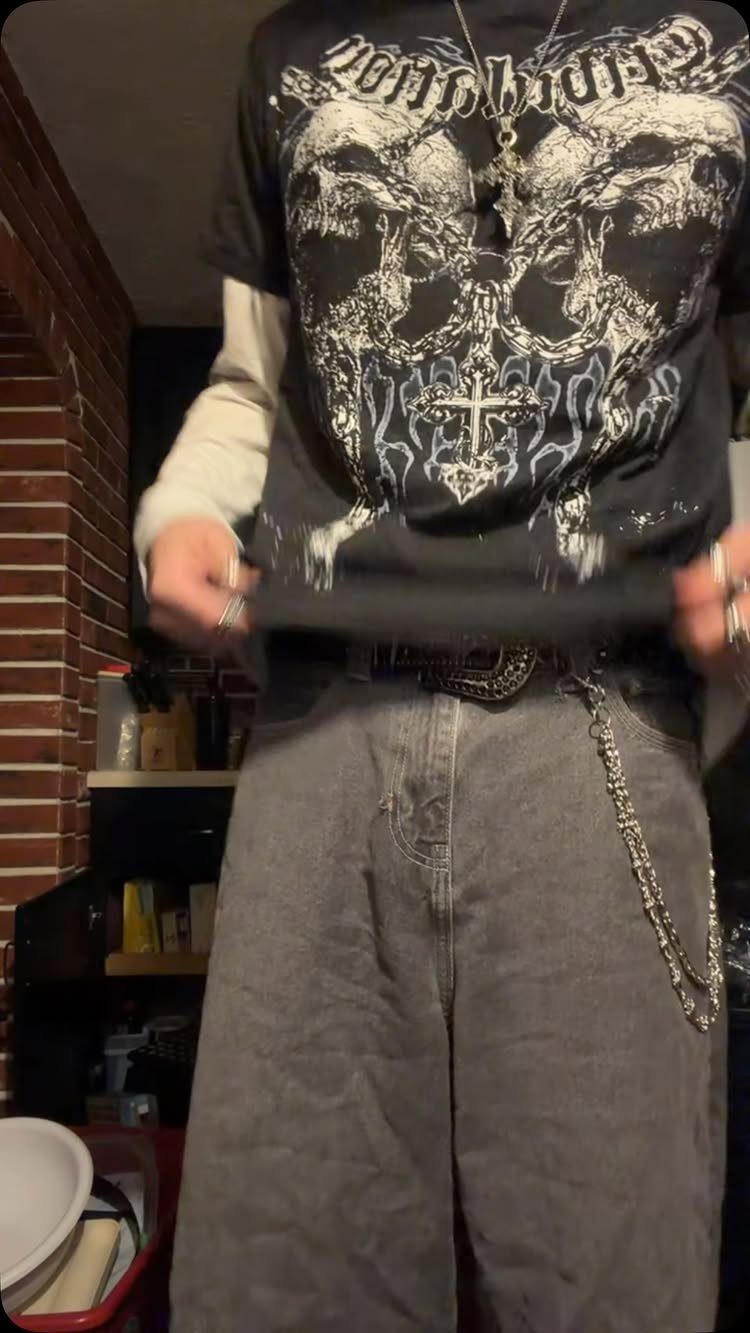 Person wearing a skull graphic tee, baggy grey jeans, and a silver wallet chain.