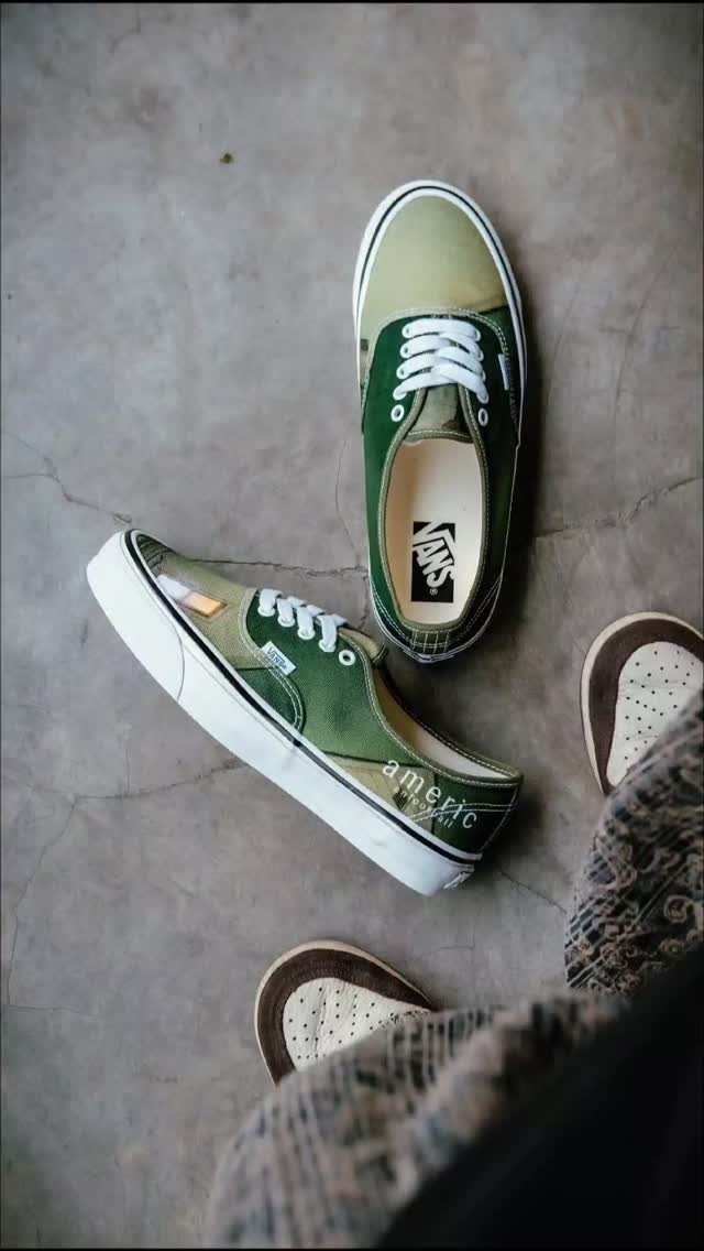Green and tan canvas Vans sneakers resting on a grey concrete floor next to patterned pants.
