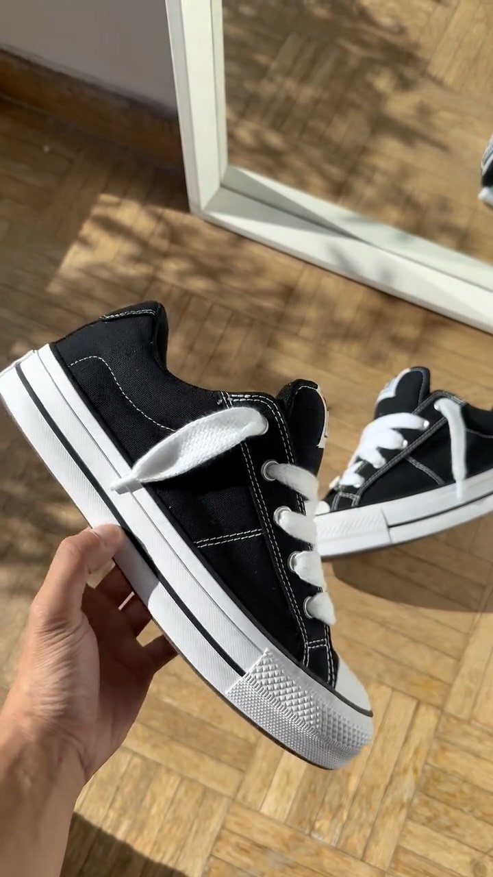 Black canvas low-top sneakers with white laces and soles held by a hand.