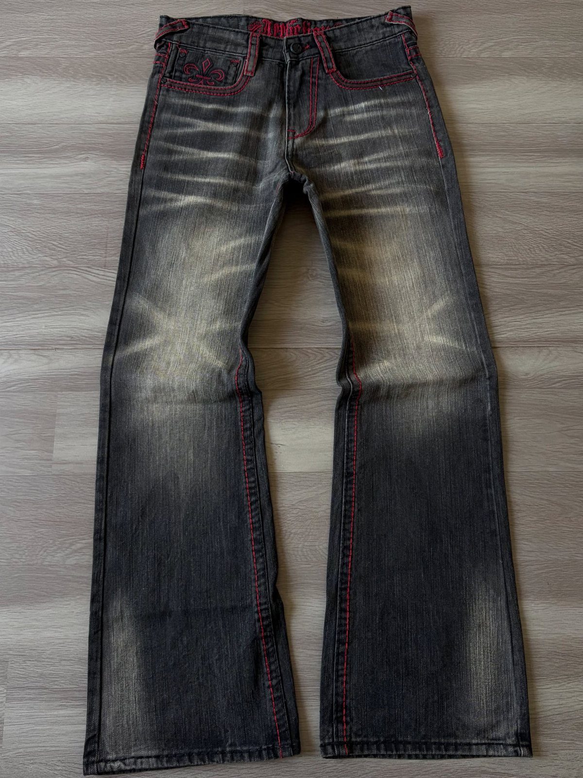 Dark grey flared denim jeans with red stitching laid flat on a grey wooden floor.