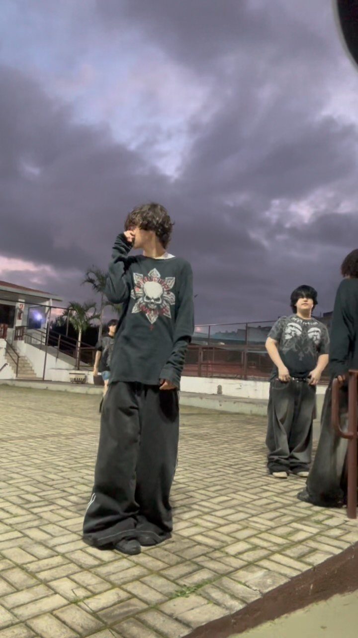 Young people in dark oversized clothing standing outdoors under a dramatic cloudy sky.