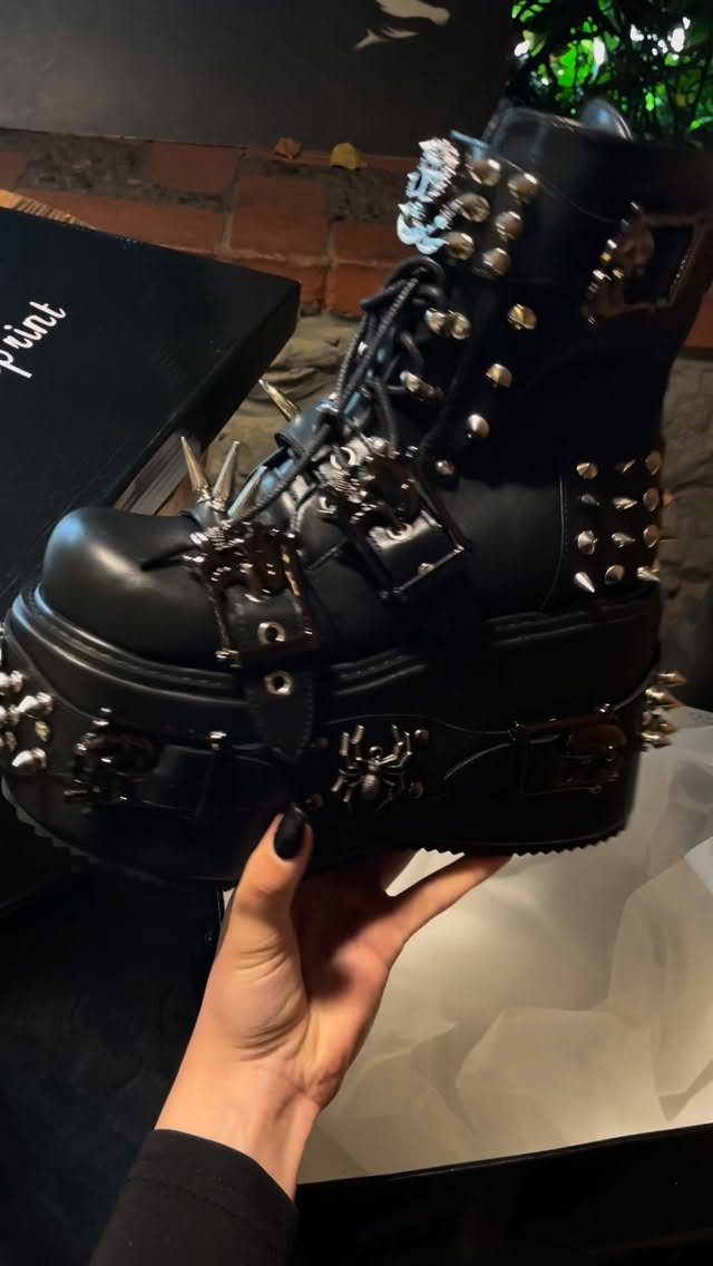 A hand holding a black platform combat boot decorated with silver metal spikes and studs.