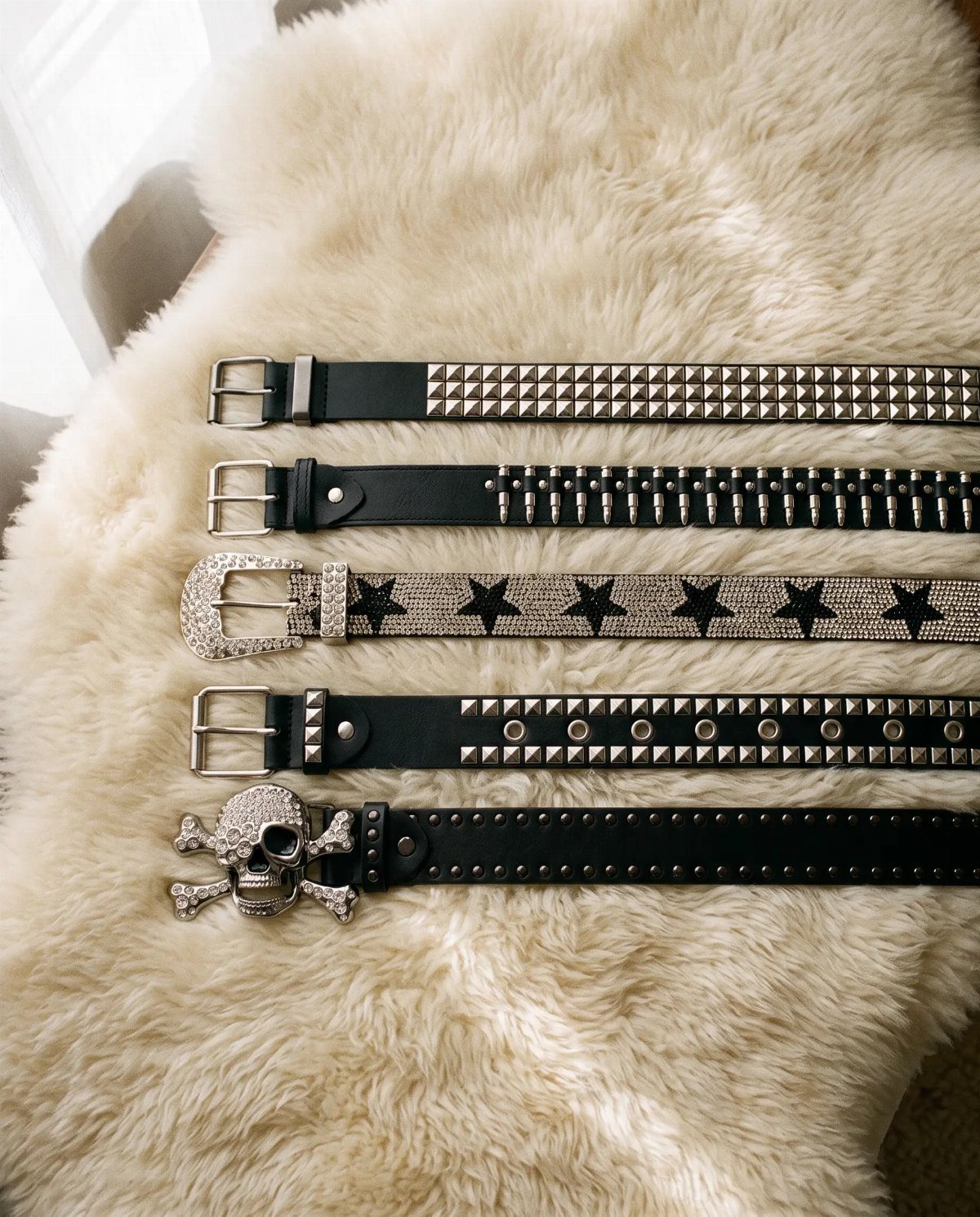 Five black studded and decorated belts resting on a white fluffy faux fur background.