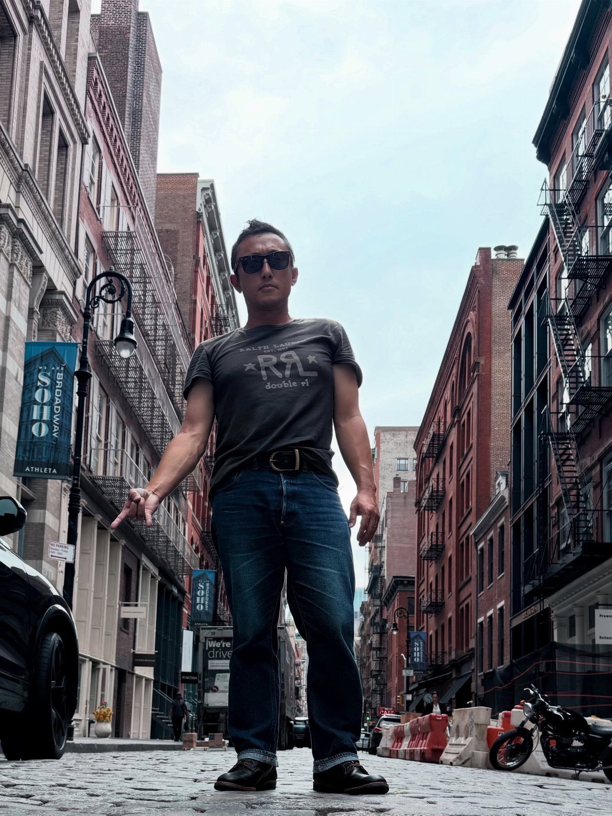 A man in a graphic t-shirt and blue jeans standing on a cobblestone city street.