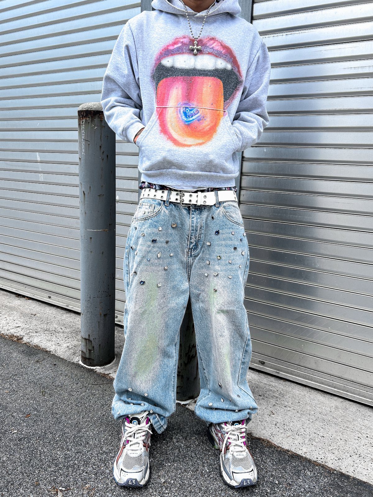 Person wearing a graphic grey hoodie, embellished baggy jeans, and chunky sneakers standing outdoors.