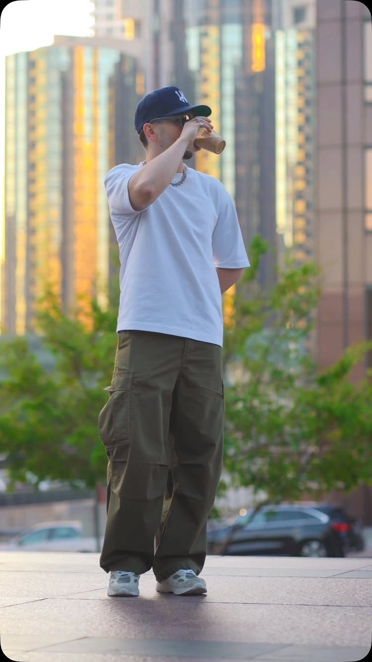 Man wearing a white t-shirt, olive cargo pants, and a blue cap in a city.