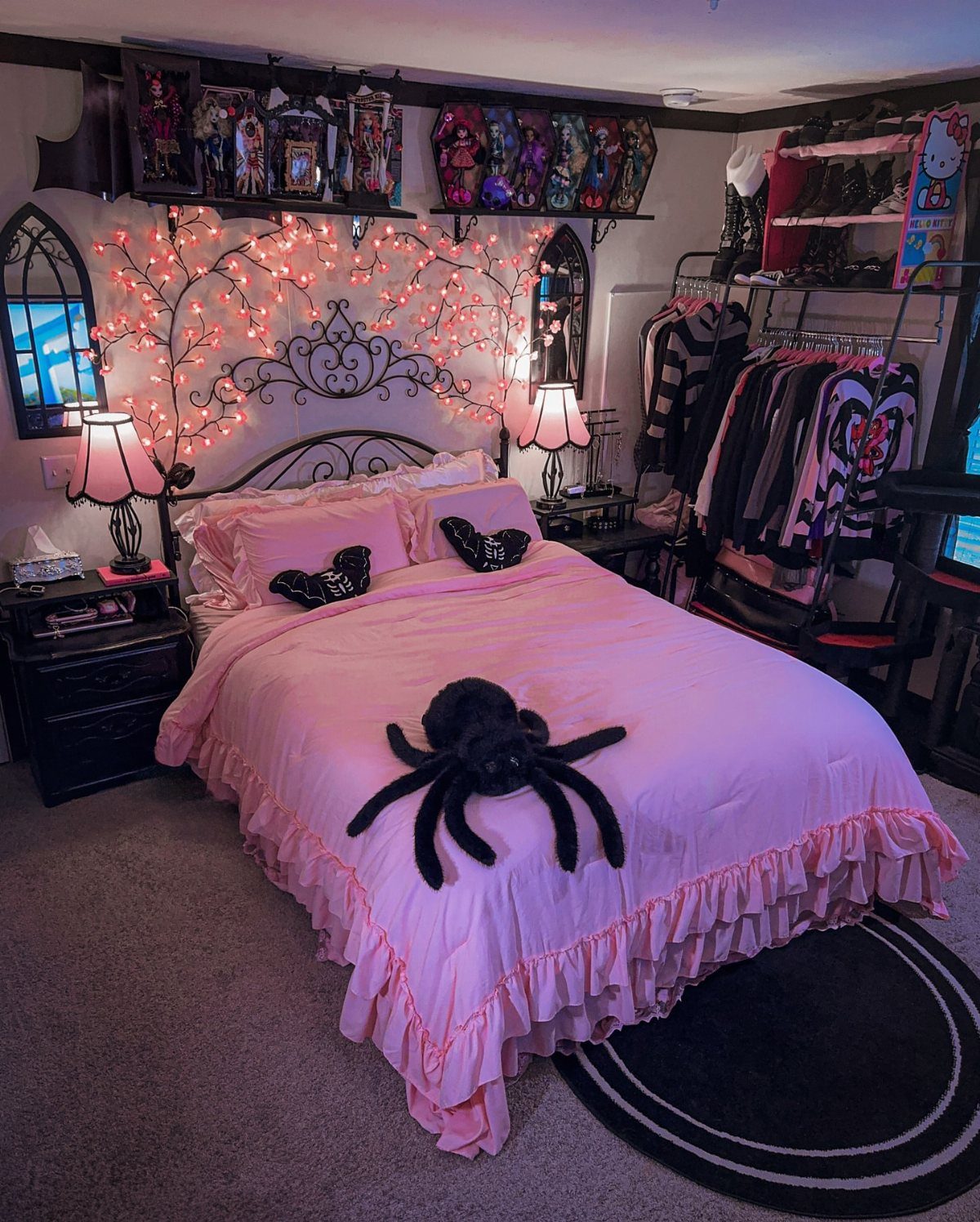A pink bed with a large black spider plush sits under fairy lights and gothic decor.