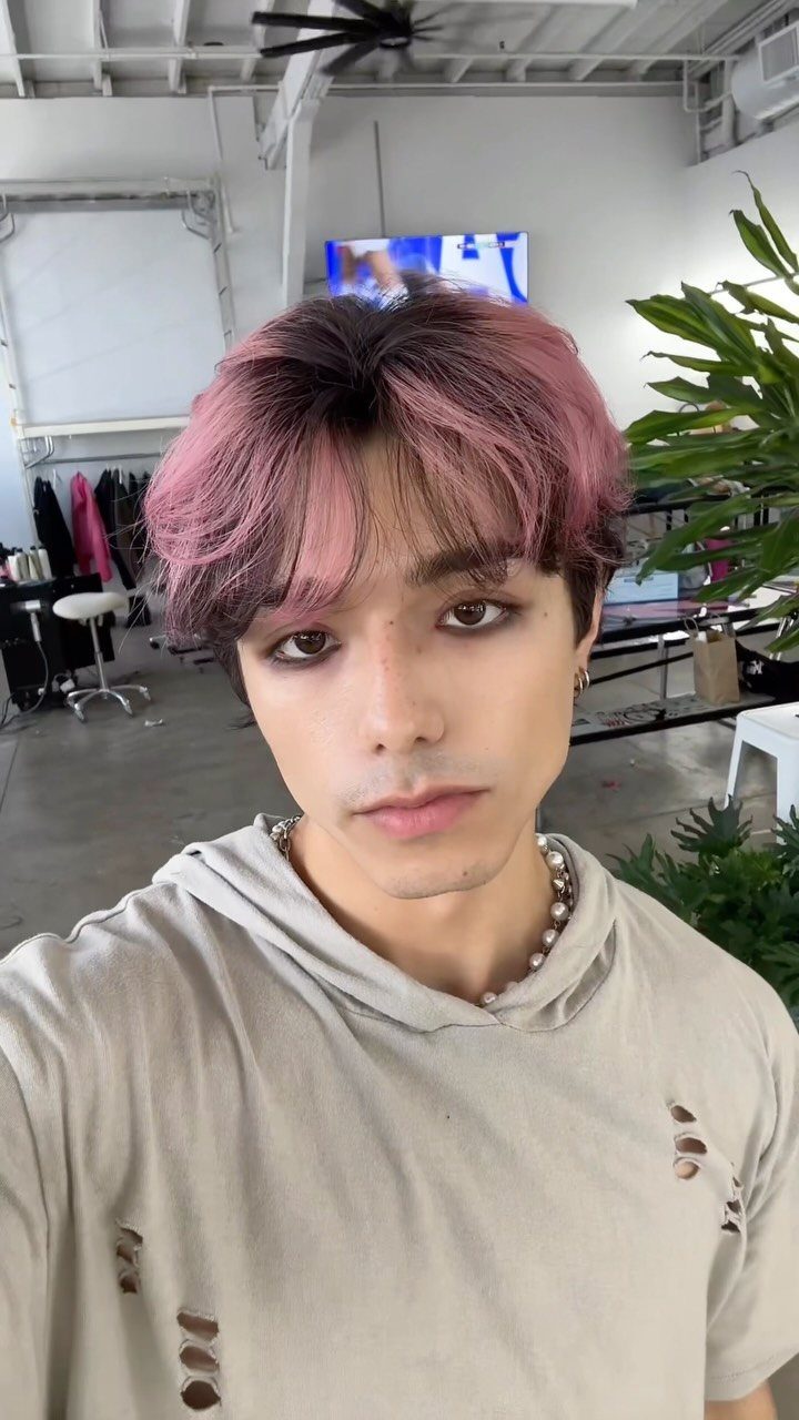 A person with dark hair featuring pastel pink ombre streaks and dyed sections.