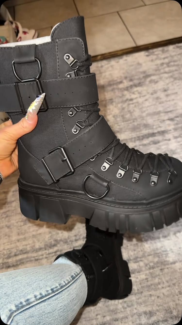 A hand holding a black platform combat boot with multiple buckles and thick soles.