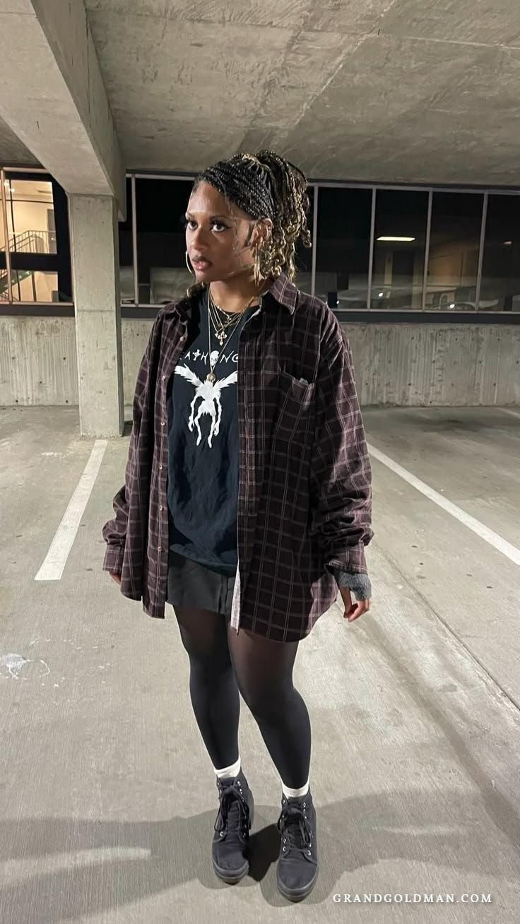 Woman in a dark plaid flannel shirt and graphic tee standing in a parking garage.