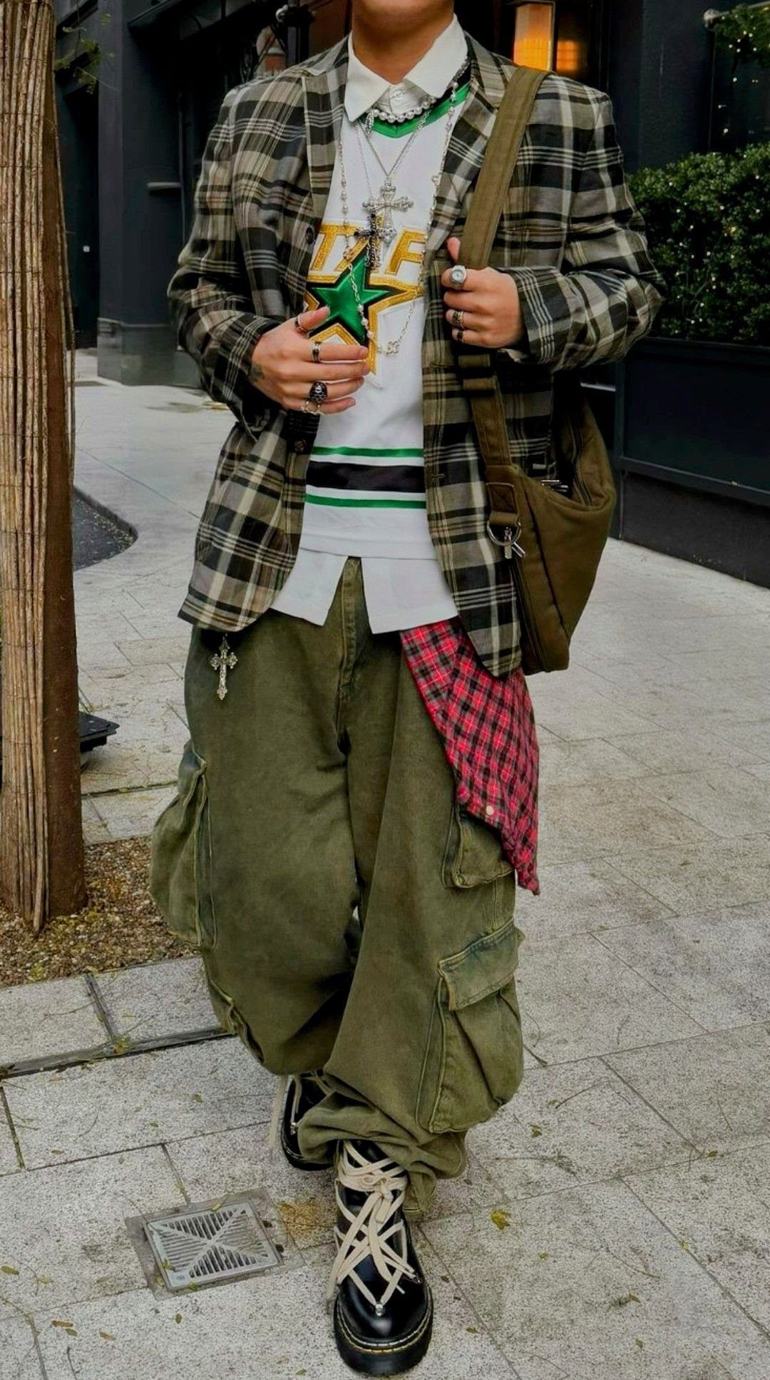 Person wearing a plaid shirt, graphic t-shirt, and olive green cargo pants with a red checkered shirt tied at the waist.